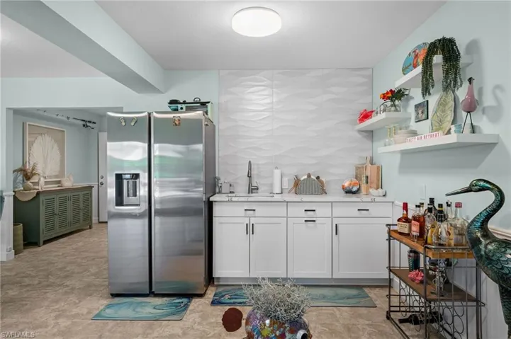 Kitchen with stainless steel refrigerator with ice dispenser, decorative backsplash, white cabinetry, open shelves, and light stone countertops