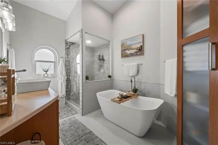 Full bathroom with double vanity, a freestanding tub, a stall shower, tile walls, and light tile patterned flooring