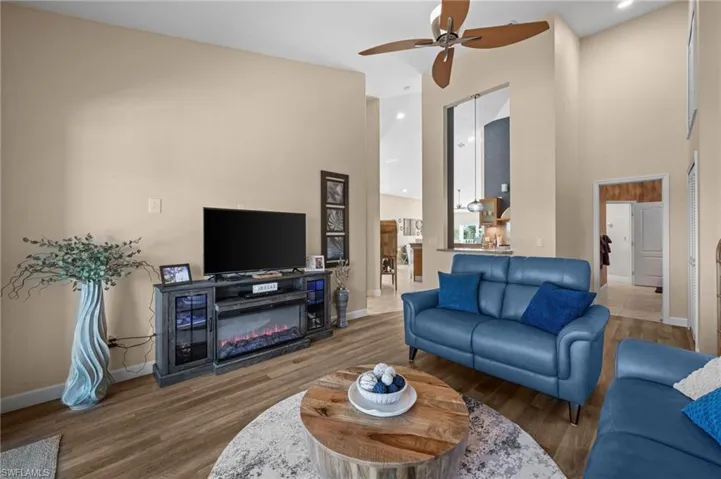 Living area featuring a towering ceiling, wood finished floors, a glass covered fireplace, and ceiling fan