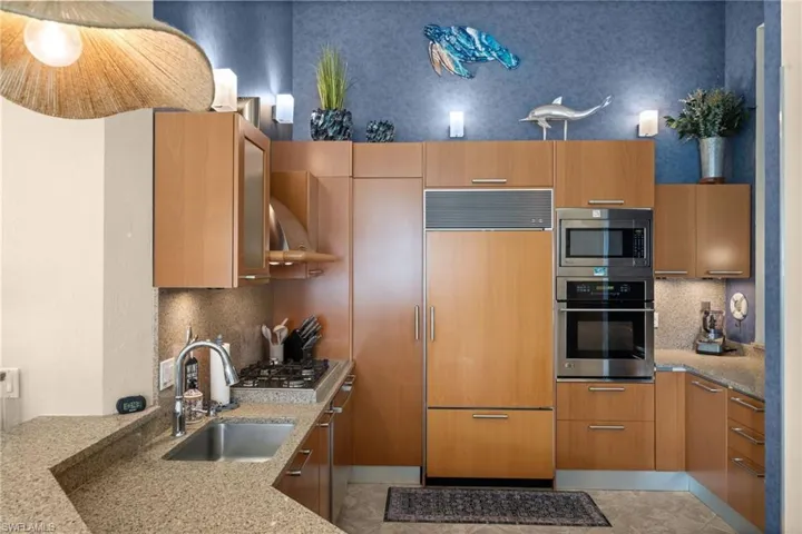 Kitchen with tasteful backsplash, light stone countertops, built in appliances, modern cabinets, and under cabinet range hood