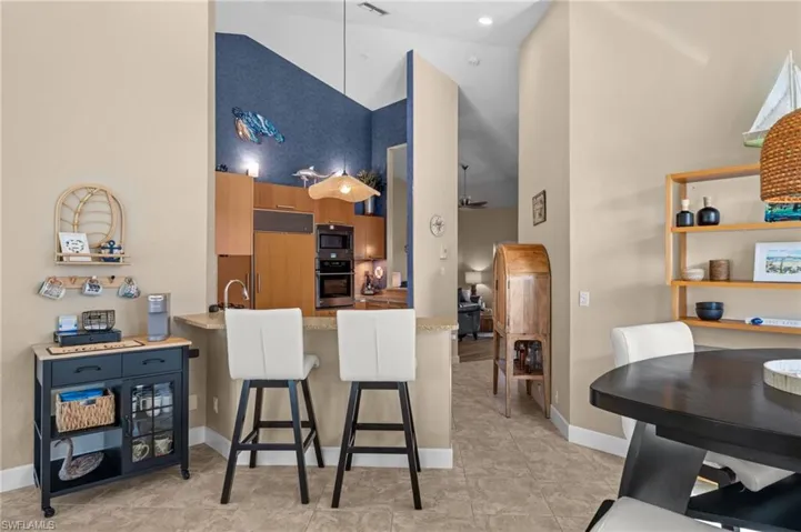 Kitchen featuring a towering ceiling, a breakfast bar area, built in appliances, brown cabinets, and a peninsula