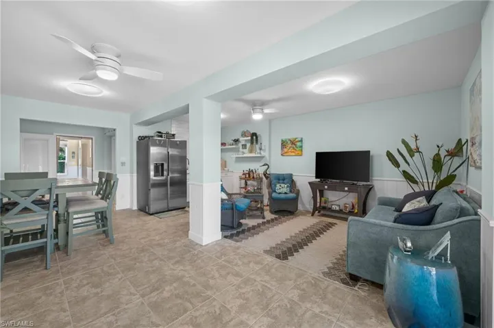 Tiled living area featuring a ceiling fan and a wainscoted wall