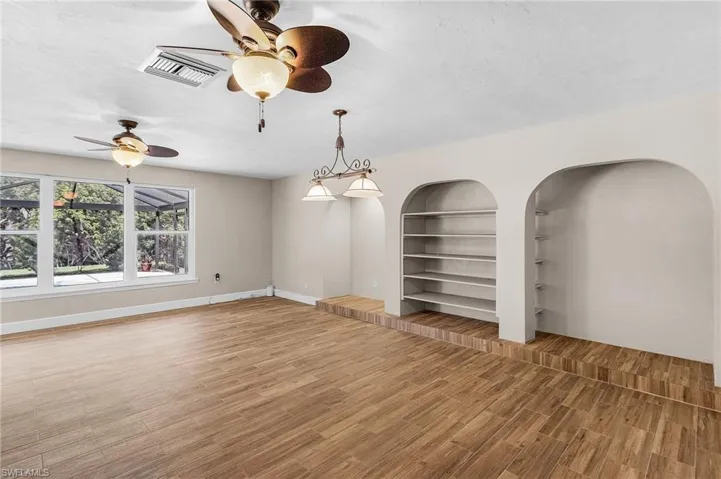 Empty room with wood finished floors, ceiling fan, built in features, and arched walkways