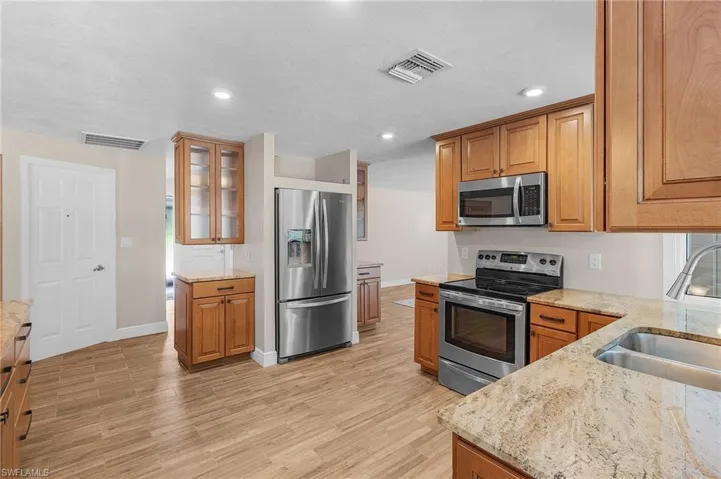 Kitchen featuring stainless steel appliances, light stone counters, brown cabinetry, glass insert cabinets, and recessed lighting