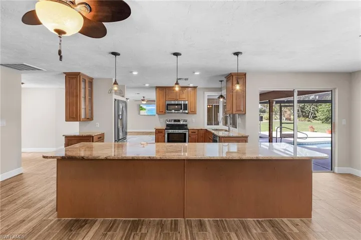 Kitchen featuring appliances with stainless steel finishes, ceiling fan, brown cabinetry, light wood-style flooring, and light stone countertops