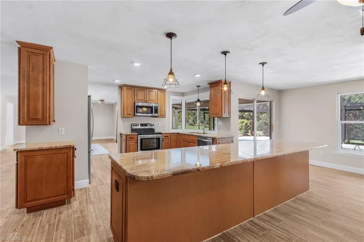 Kitchen featuring stainless steel appliances, light wood finished floors, light stone counters, and brown cabinets