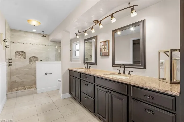 Bathroom featuring double vanity, a walk in shower, tile patterned floors, and rail lighting