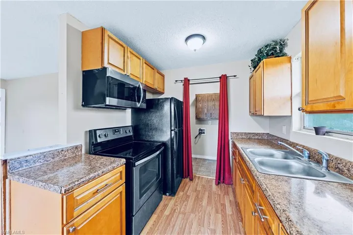 Kitchen with light wood-type flooring, appliances with stainless steel finishes, a textured ceiling, and sink