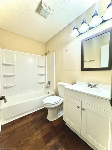 Full bathroom featuring toilet, vanity, a textured ceiling, shower / bathing tub combination, and wood-type flooring