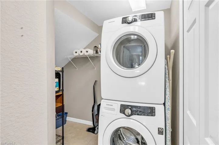 Laundry area featuring stacked washer and clothes dryer, a textured wall, and light tile patterned floors