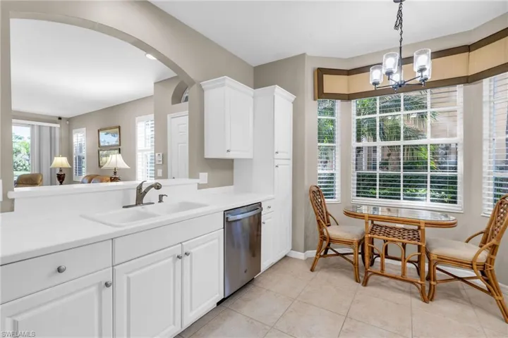 Kitchen with stainless steel dishwasher, a chandelier, light countertops, hanging light fixtures, and white cabinetry