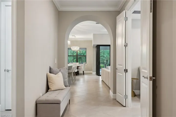Corridor featuring light tile patterned flooring, crown molding, and an inviting chandelier