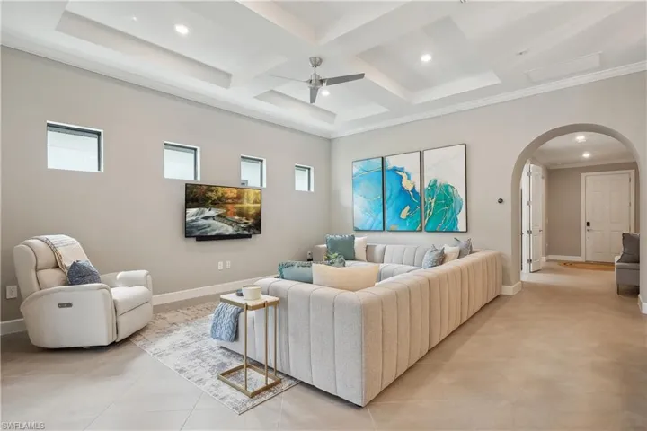 Tiled living room with ceiling fan, crown molding, coffered ceiling, and beamed ceiling