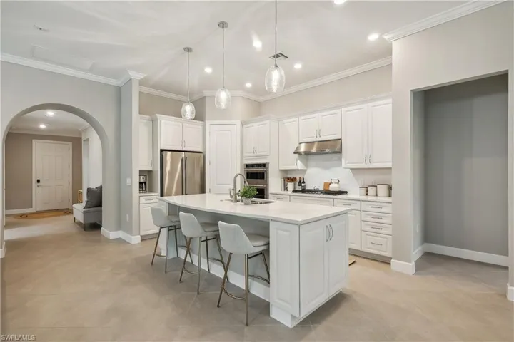 Kitchen featuring white cabinets, hanging light fixtures, ornamental molding, a kitchen island with sink, and stainless steel appliances