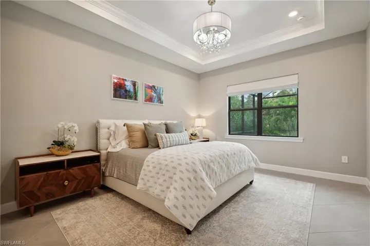 Bedroom featuring crown molding, an inviting chandelier, light tile patterned floors, and a tray ceiling