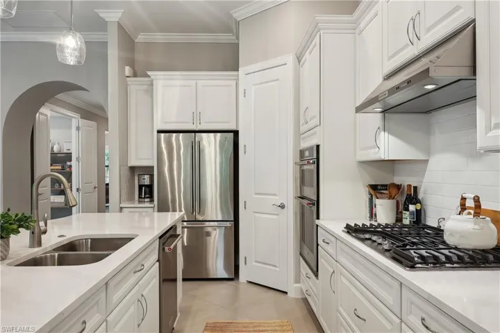 Kitchen with light tile patterned flooring, sink, stainless steel appliances, and white cabinets