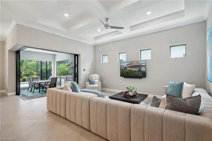 Tiled living room featuring coffered ceiling, beamed ceiling, ornamental molding, and ceiling fan
