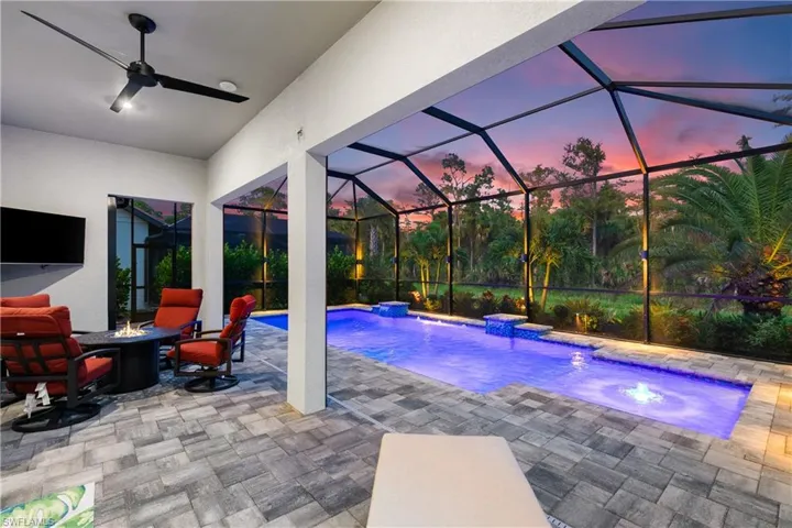 Pool at dusk featuring ceiling fan, a patio, pool water feature, glass enclosure, and a hot tub