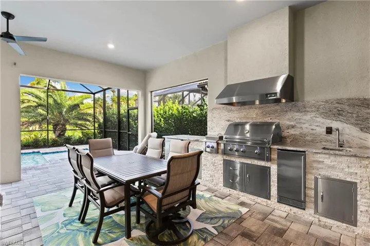 View of patio featuring ceiling fan, glass enclosure, an outdoor kitchen, sink, and area for grilling
