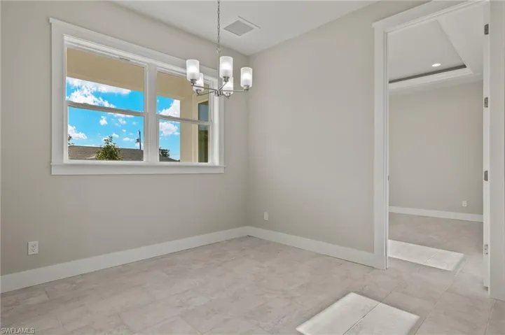 Empty room featuring a raised ceiling, an inviting chandelier, and light tile patterned flooring