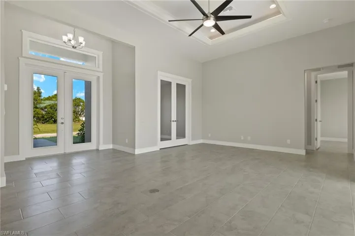 Spare room featuring french doors, ceiling fan with notable chandelier, a tray ceiling, and light tile patterned floors
