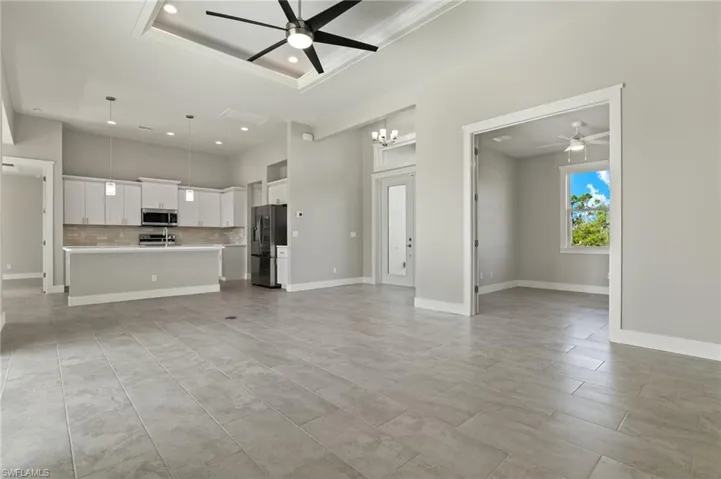 Unfurnished living room featuring a raised ceiling, ceiling fan with notable chandelier, and light tile patterned flooring