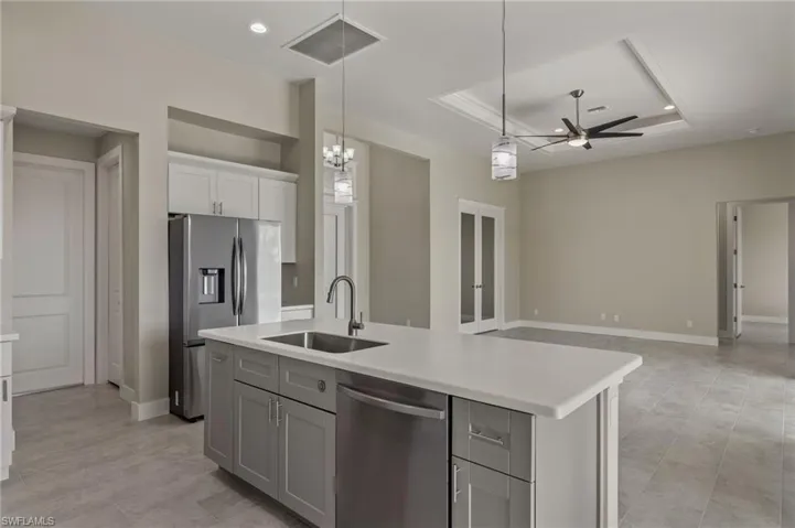 Kitchen with sink, a raised ceiling, ceiling fan with notable chandelier, and an island with sink