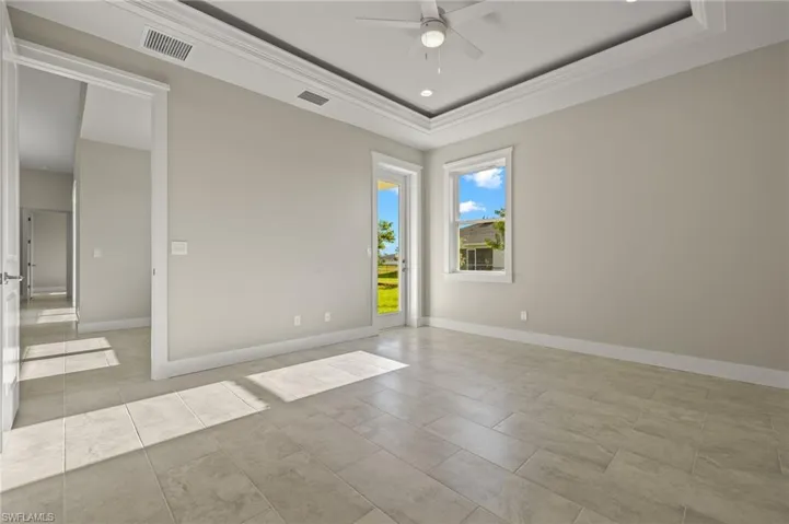 Tiled empty room featuring ceiling fan and a raised ceiling