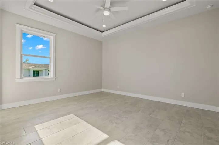 Spare room featuring a tray ceiling, ceiling fan, and light tile patterned flooring