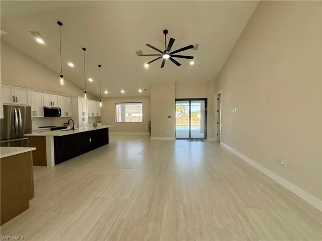 Kitchen with lofted ceiling, open floor plan, stainless steel appliances, a center island with sink, and a ceiling fan
