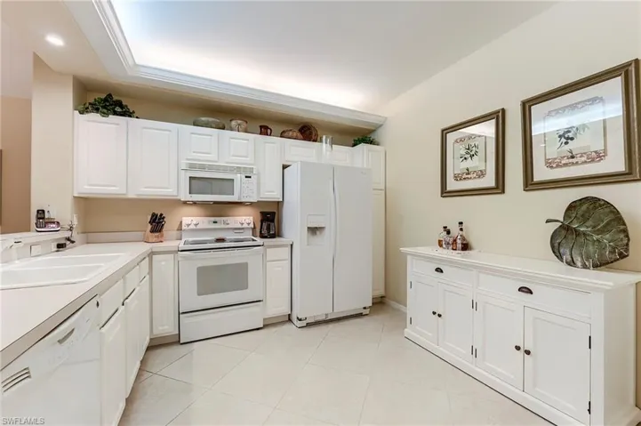Kitchen with white appliances, white cabinetry, light countertops, a sink, and light tile patterned floors