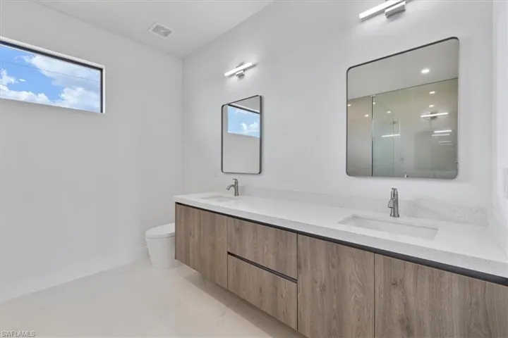 Full bathroom with toilet, a sink, double vanity, and visible vents