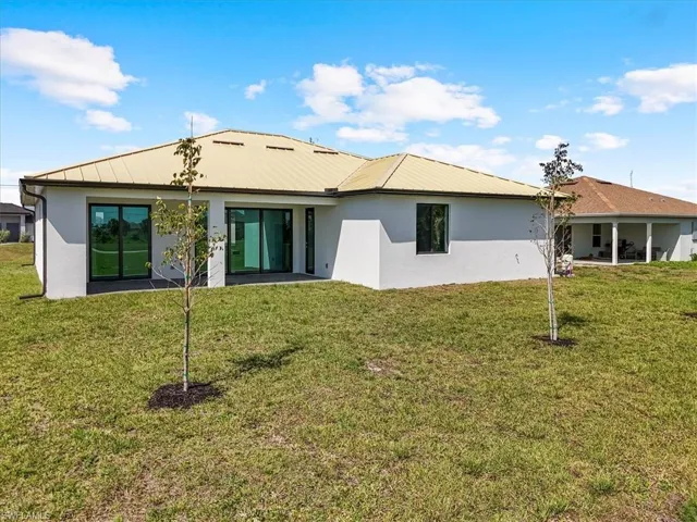 Back of house featuring stucco siding, metal roof, and a yard
