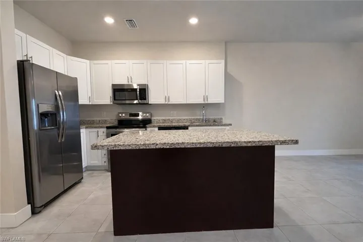 Kitchen featuring white cabinets, stainless steel appliances, light stone counters, a center island, and light tile patterned floors