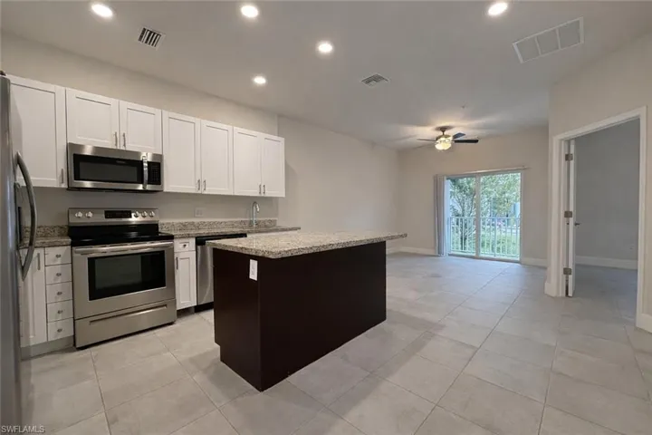 Kitchen with stainless steel appliances, a kitchen island, recessed lighting, ceiling fan, and light stone counters
