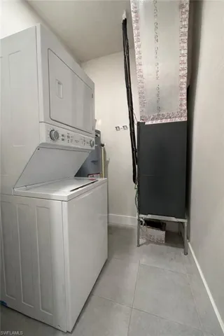 Laundry area with heating unit, stacked washer and clothes dryer, and light tile patterned flooring