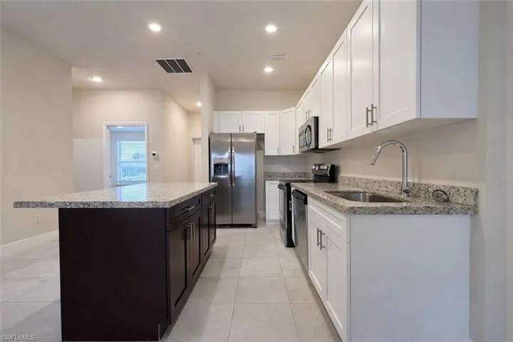 Kitchen featuring light stone countertops, stainless steel appliances, a center island, two tone color scheme, and recessed lighting