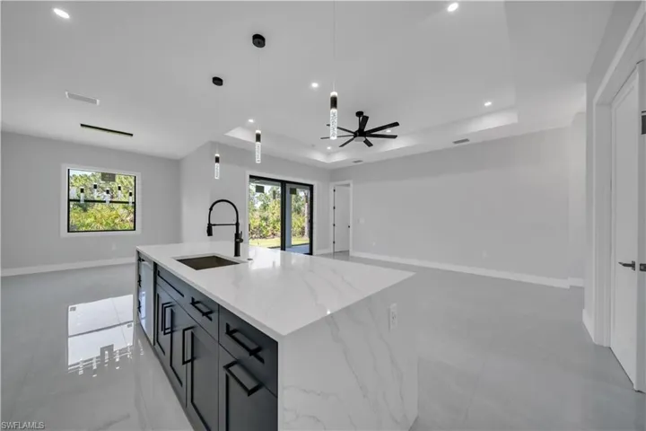 Kitchen featuring a sink, open floor plan, a raised ceiling, recessed lighting, and baseboards