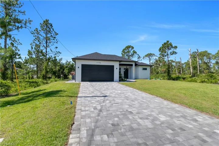 View of front of home featuring decorative driveway, an attached garage, a front lawn, and stucco siding