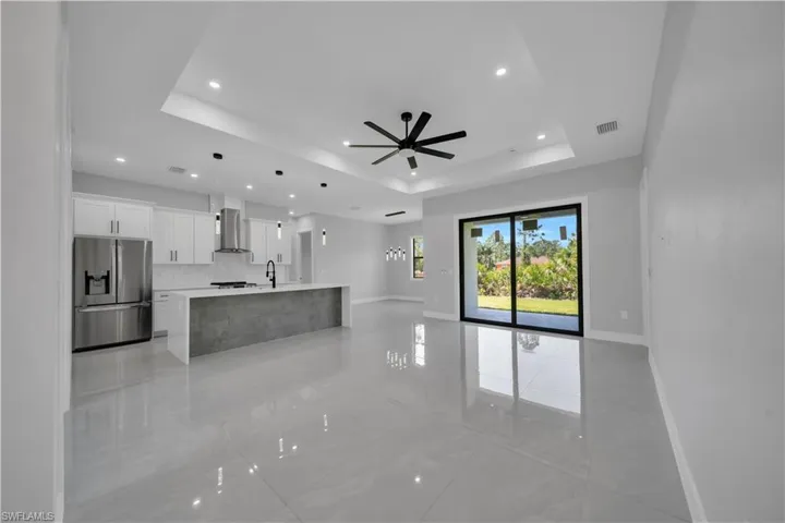 Unfurnished living room featuring a tray ceiling, recessed lighting, ceiling fan, baseboards, and a sink