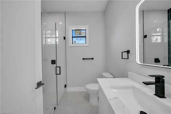 Bathroom with toilet, a stall shower, vanity, and marble finish flooring