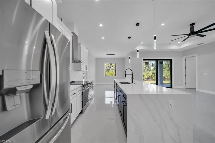 Kitchen featuring appliances with stainless steel finishes, a sink, wall chimney exhaust hood, a kitchen island with sink, and recessed lighting