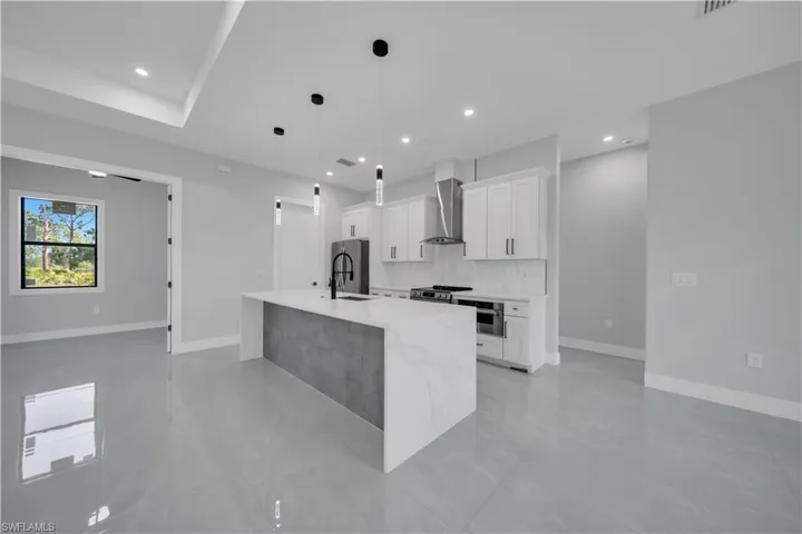 Kitchen with stainless steel appliances, a sink, white cabinetry, a center island with sink, and recessed lighting