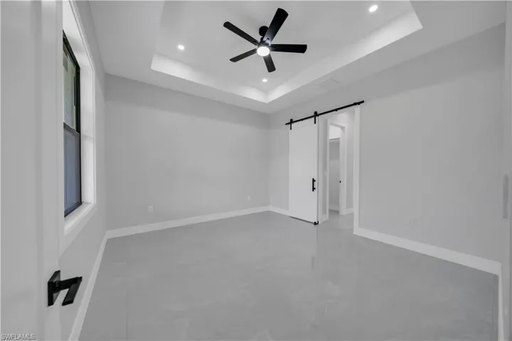 Empty room with ceiling fan, recessed lighting, a barn door, a tray ceiling, and baseboards