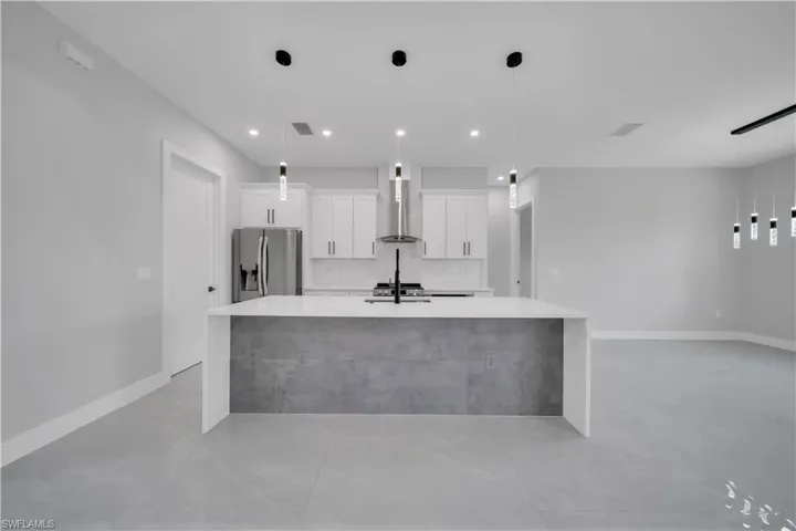 Kitchen featuring stainless steel fridge with ice dispenser, a large island with sink, wall chimney range hood, light countertops, and white cabinetry