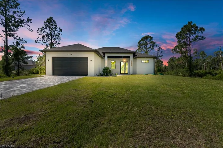 View of front of home with a garage, stucco siding, decorative driveway, and a front lawn