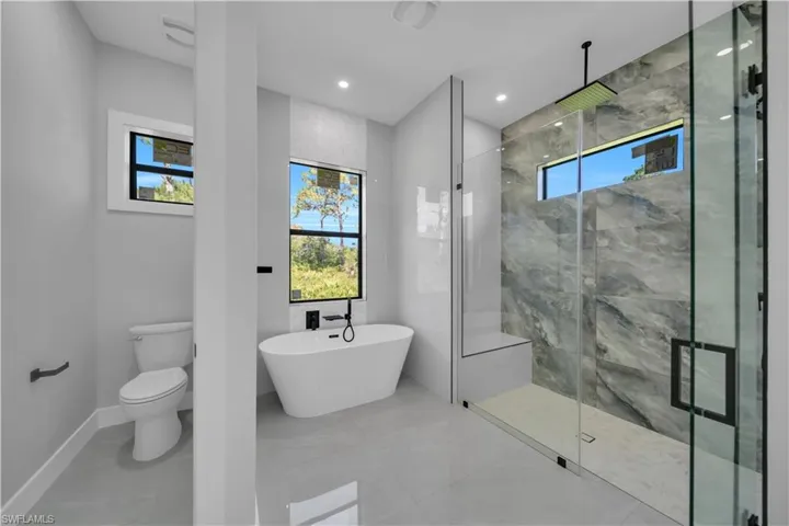 Full bathroom with a shower stall, a soaking tub, toilet, baseboards, and marble finish floors