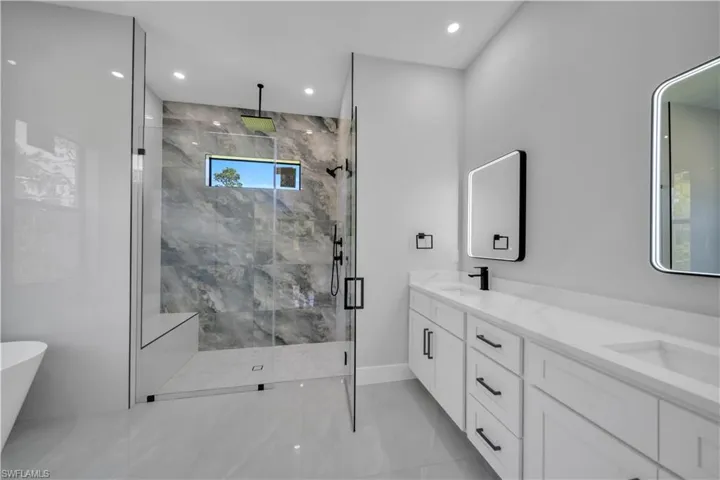 Bathroom with marble finish flooring, a shower stall, double vanity, a freestanding bath, and baseboards