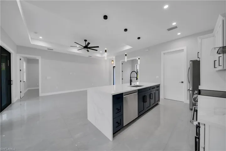 Kitchen with appliances with stainless steel finishes, a center island with sink, a sink, a ceiling fan, and white cabinetry