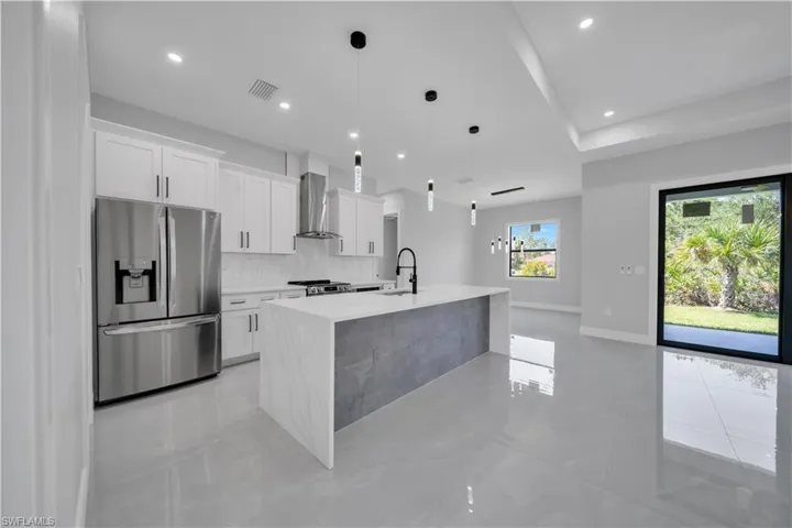 Kitchen featuring appliances with stainless steel finishes, wall chimney range hood, a sink, light countertops, and recessed lighting